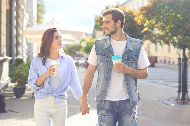 Image of young couple man and woman in casual clothes drinking takeaway coffee while strolling through city street. - Fotografie, Obrázek