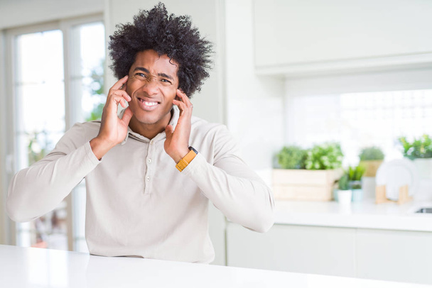 Αφρικανική αμερικανική άνδρα στο σπίτι που καλύπτουν τα αυτιά με τα δάχτυλα με ενοχλημένος έκφραση για το θόρυβο δυνατά μουσική. Κωφών έννοια. - Φωτογραφία, εικόνα