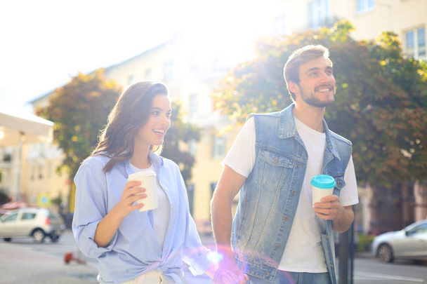 Image of young couple man and woman in casual clothes drinking takeaway coffee while strolling through city street. - Foto, imagen