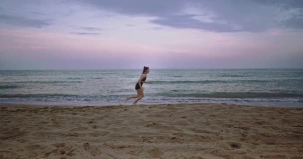 Op een grote strand kant sportieve dame beginnen te rennen in de ochtend naast de zee zeer geconcentreerd, geweldig uitzicht op de hemel - Video