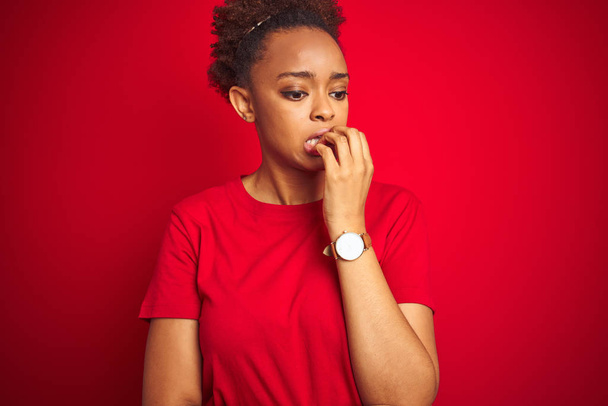 Young beautiful african american woman with afro hair over isolated red background looking stressed and nervous with hands on mouth biting nails. Anxiety problem. - Фото, изображение