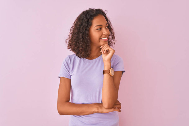 Young brazilian woman wearing t-shirt standing over isolated pink background with hand on chin thinking about question, pensive expression. Smiling and thoughtful face. Doubt concept. - Foto, imagen