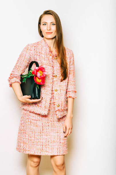 Fashion portrait of beautidul young woman wearing pink tweed suit, holding black leather bag with peony flowers - Photo, Image