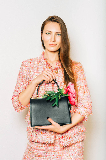 Fashion portrait of beautidul young woman wearing pink tweed suit, holding black leather bag with peony flowers - Foto, immagini