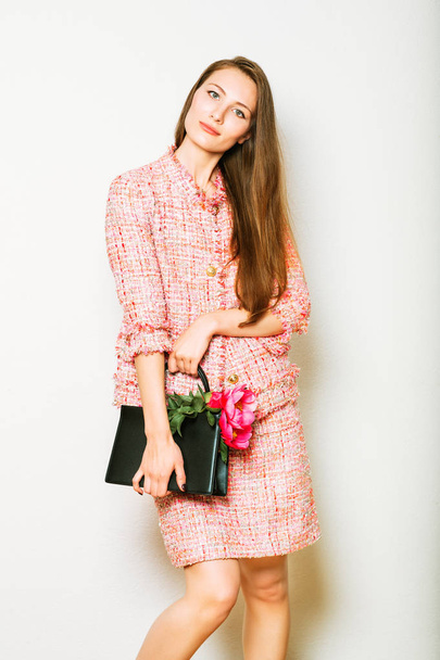 Fashion portrait of beautidul young woman wearing pink tweed suit, holding black leather bag with peony flowers - Valokuva, kuva