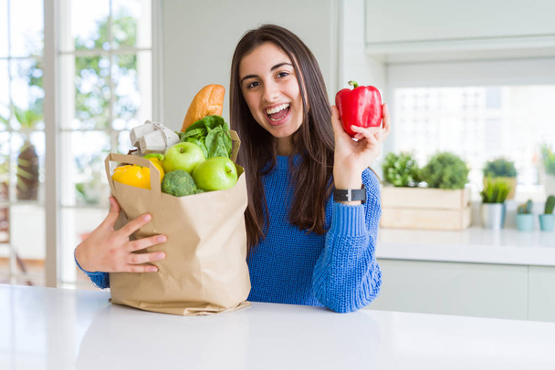Young beautiful woman smiling holding a paper bag full of grocer - Foto, imagen
