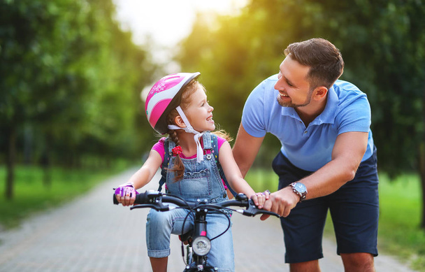ευτυχισμένος οικογένεια πατέρας διδάσκει παιδί κόρη να οδηγήσετε ένα ποδήλατο στο - Φωτογραφία, εικόνα