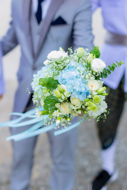 der junge Mann ist verliebt. hält einen weißen Strauß, um einem geliebten Wonan auf grünem Bokeh-Hintergrund zu schenken. glückliches Warten, stilvoller Bräutigam mit Blumenstrauß.  - Foto, Bild