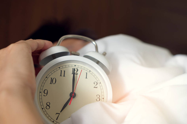 Alarm clock on bedside table with woman sleeping on background - Φωτογραφία, εικόνα