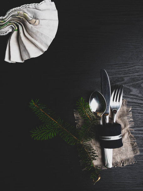 Χριστουγεννιάτικο φόντο φαγητού. Μαχαίρι, πιρούνι, κλαδί ερυθρελάτης σε ένα μαύρο ξύλινο τραπέζι, τονισμένη κορυφή, επίπεδη θέση, αντίγραφο χώρου - Φωτογραφία, εικόνα