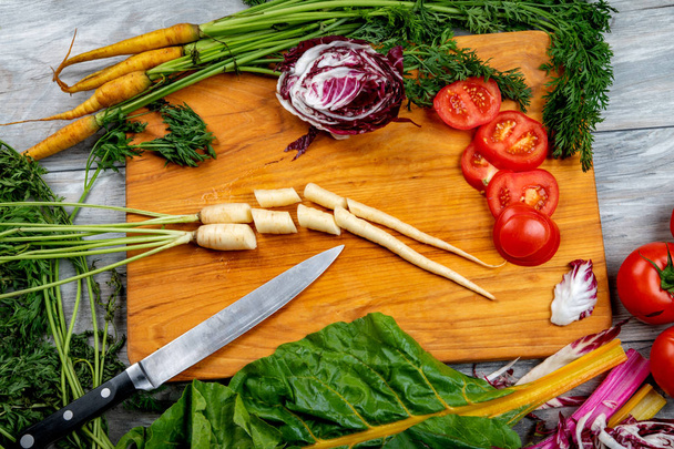 Szeletelt zöldségek egy fa vágódeszka késsel - Fotó, kép