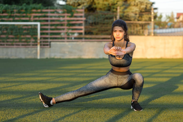 A young slim athletic girl in sportswear with snakeskin prints performs a set of exercises. Fitness and healthy lifestyle. - Фото, изображение