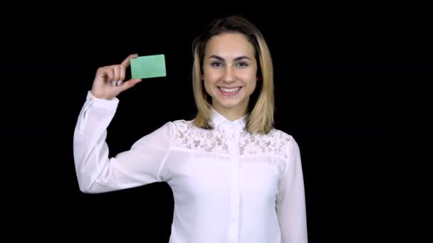Young businesswoman in a white shirt holds a bank card in her hand. Isolated black background. Chromakey green card. 4k - Video