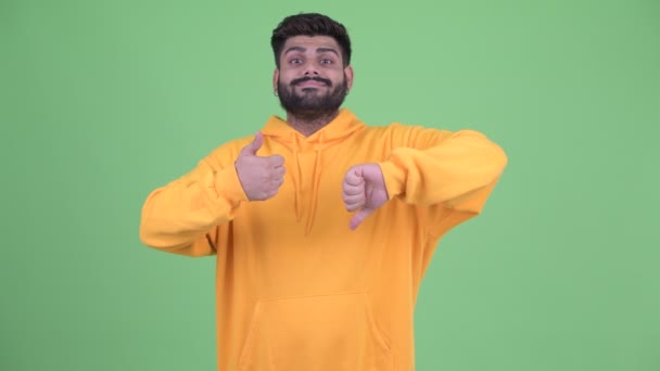 Mylić młody nadwaga Brodaty indyjski mężczyzna wybór między kciuki w górę i kciuki w dół - Materiał filmowy, wideo