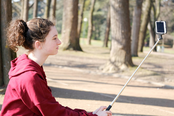 teenager girl making photo with selfie stick outside near lake - Photo, Image
