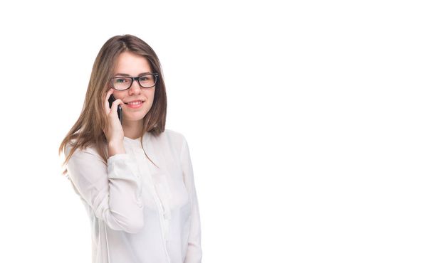 Smiling businesswoman in glasses talking on mobile phone. Beautiful young girl in white shirt on white isolated background talking on mobile phone. Woman in shirt with cellphone. Copy space. Blank - Photo, image