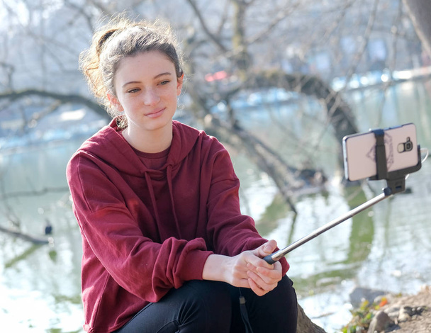 10代の女の子が湖の近くで自撮り棒で写真を撮る - 写真・画像