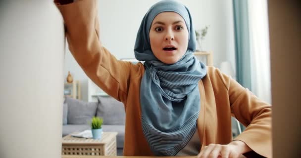 Surprised Middle Eastern woman in hijab opening carton box taking gift smiling - Filmagem, Vídeo