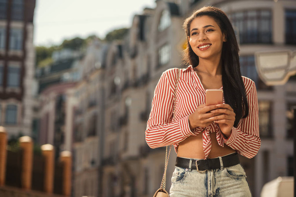 Lady with smartphone. Happy young lady in casual summer clothes looking away with a smile while holding smartphone - Foto, immagini
