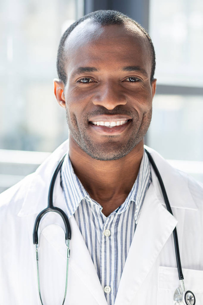 Portrait photo. Cheerful young man keeping stethoscope around neck and looking forward while posing on camera - Fotoğraf, Görsel