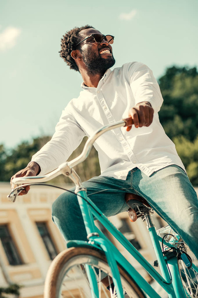 Positiver Mann auf blauem Fahrrad dreht Kopf und lächelt - Foto, Bild