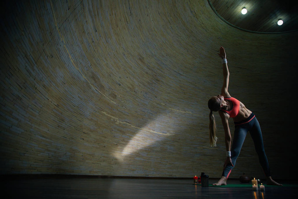 Длинноволосая молодая женщина практикующая йогу в сферической комнате и делающая треугольную позу одной рукой вверх. Копирование пространства слева
 - Фото, изображение