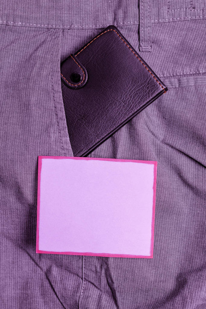 kleines Portemonnaie in der Hosentasche neben lila Zettelchen. Eine kleine Handtasche ist in der Hose des Mannes in der Nähe des Notenblattes verstaut. Künstlerische Art und Weise, flache Laienfotografie zu arrangieren - Foto, Bild