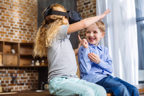 Virtual gadget. Cheerful positive little siblings using VR glasses while having fun at home - Fotó, kép