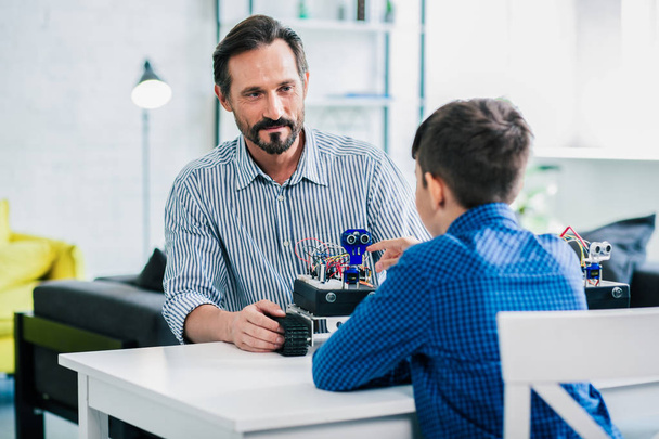 Handsome smiling man sitting at the table with his son while working on robotic project - Фото, зображення