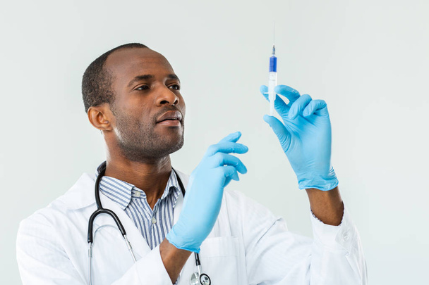 Make it painless. Serious afro maerican doctor making an injection while holding a syringe - Foto, imagen