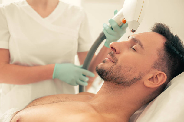 Close up photo of the man lying with closed eyes and enjoying painless laser hair removal procedure - Photo, Image