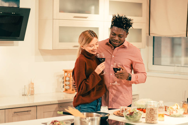 Young happy man gently hugging his girlfriend and looking at the meals on the table while enjoying wine with her - Φωτογραφία, εικόνα