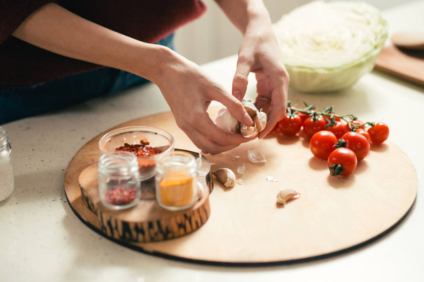 Close up of the table with cutting board on it and hands of woman holding garlic above the cherry tomatoes - Foto, immagini