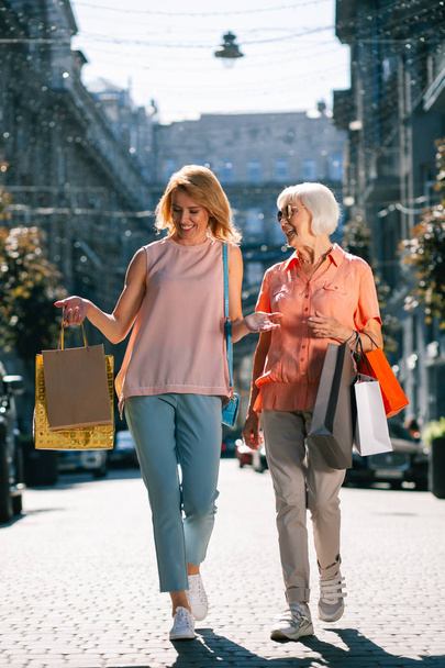 Positive elderly lady and her daughter walking with adult daughter on sunny day in the city - Foto, afbeelding