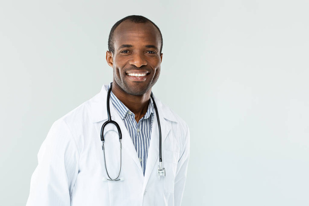 Welcoming look. Positive professional doctor smiling while standing aginst white background - Foto, imagen