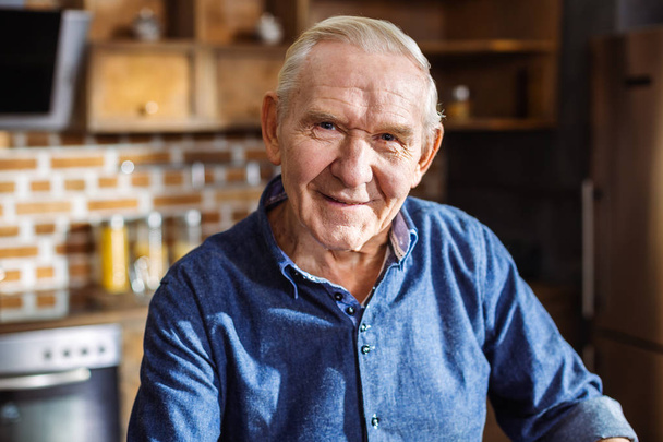Happy retirement. Close up of a joyful elderly man smiling while standing in the kitchen - Foto, afbeelding