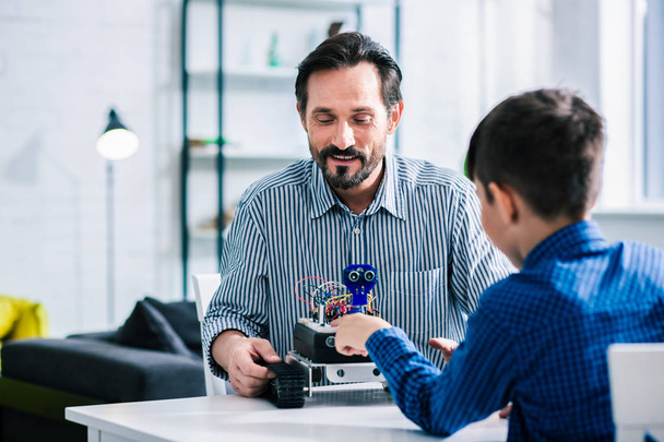 Pleasant delighted man constructing robotic device while sitting with his son - Foto, Bild