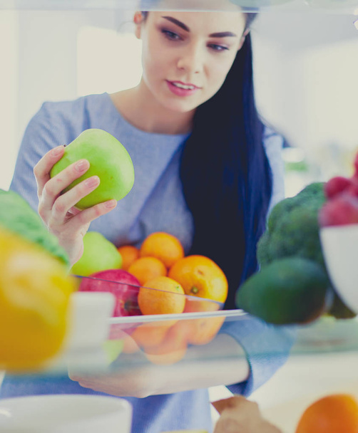 Smiling woman taking a fresh fruit out of the fridge, healthy food concept - Fotografie, Obrázek