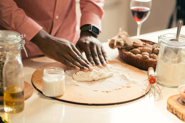Close up of the table with wooden cutting board and man putting both hands on the dough - Fotografie, Obrázek