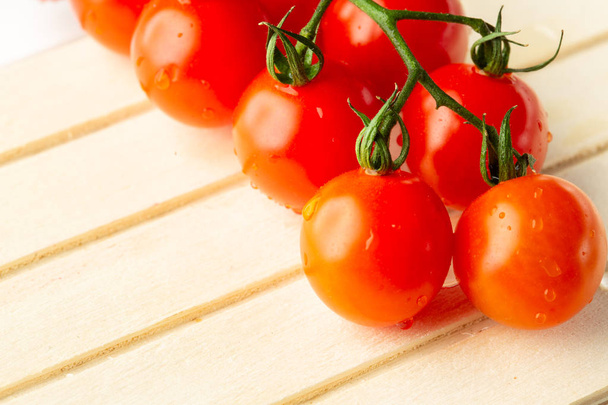 Close up photo with fresh clean cherry tomatoes with drops of water on them lying on striped wooden surface - Fotó, kép
