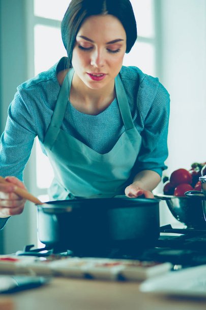 Woman standing by the stove in the kitchen, cooking and smelling the nice aromas . - Foto, imagen