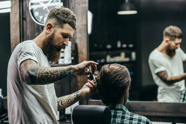 Professional barber with tattooed arms holding a comb and making haircut for his client - Foto, immagini