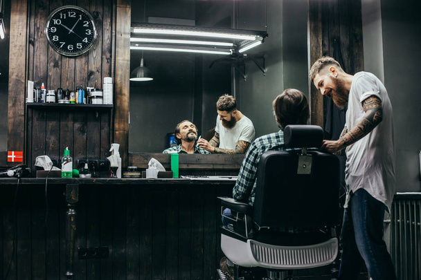 Professional friendly barber smiling and looking attentive while combing the beard of his client - 写真・画像