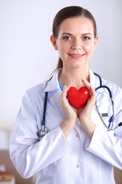 Beautiful young smiling female doctor sitting at the desk and holding heart. - Photo, Image