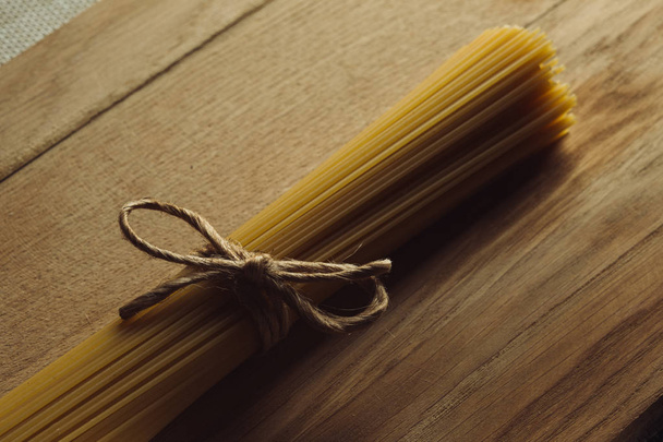 Close up of a bunch of uncooked Italian pasta tied with a rope and placed on a wooden surface - Foto, Bild