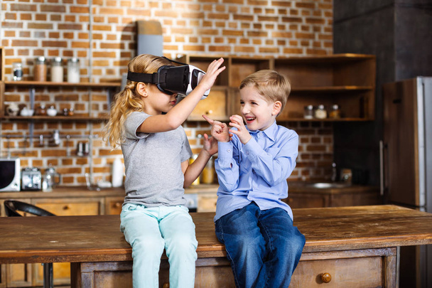 Something new. Pleasant cute little siblings using VR glasses while sitting in the kitchen - Fotó, kép