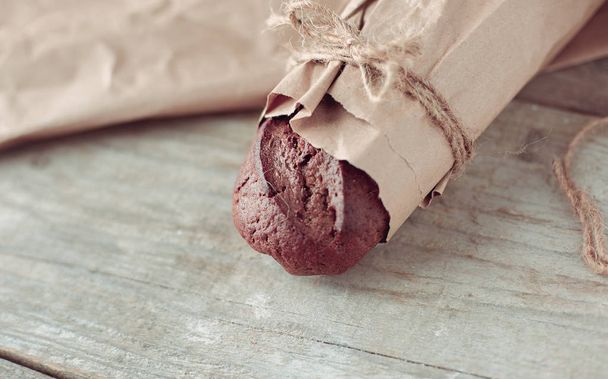 Fresh baked bread wrapped in paper, on wooden background - Photo, Image