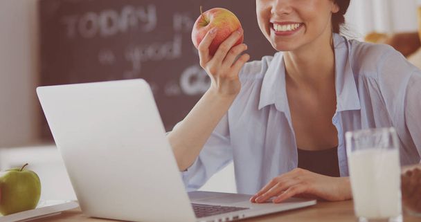 Woman with apple and laptop sitting in the kitchen - Foto, Bild