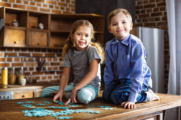 Our hobby. Cheerful little siblings sitting in the kitchen and assembling jigsaw puzzles - Foto, imagen