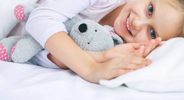 Child little girl sleeps in the bed with a toy teddy bear. - Foto, afbeelding